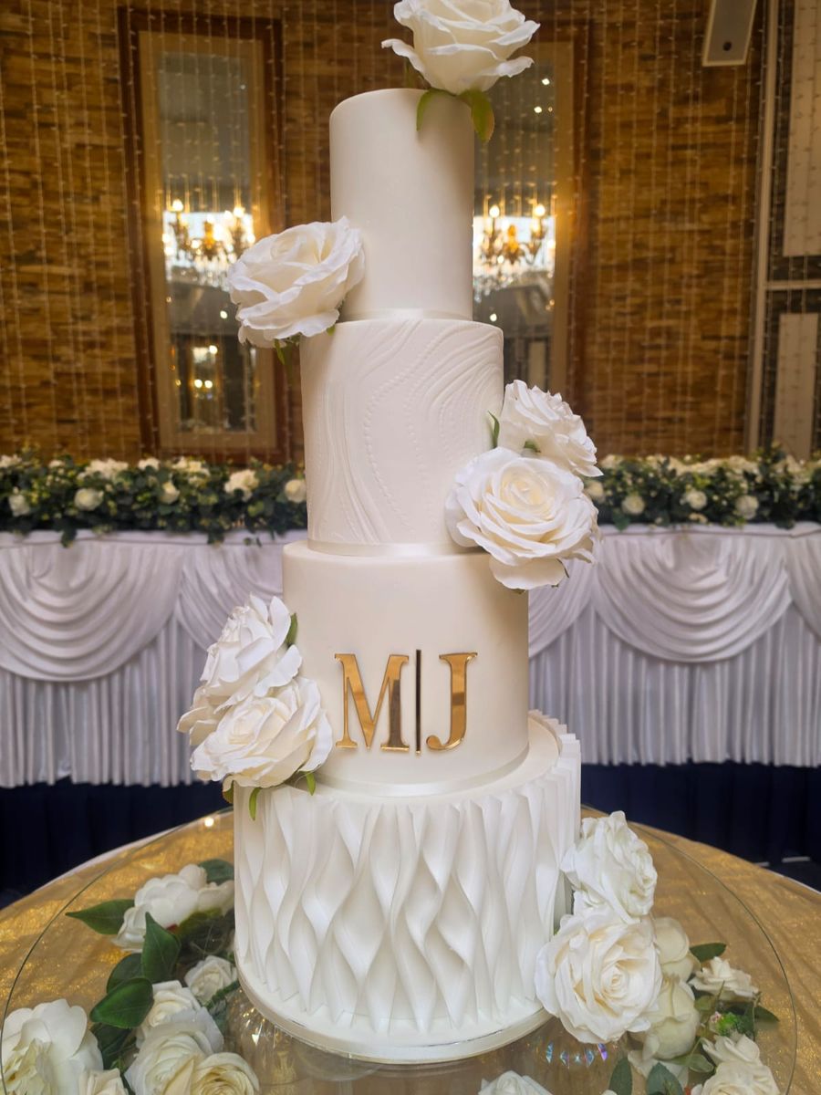 Four tier white cake with white sugar roses and a gold monogram