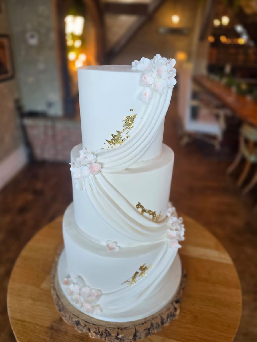 Three tier white cake with draped sugar and gold leaf