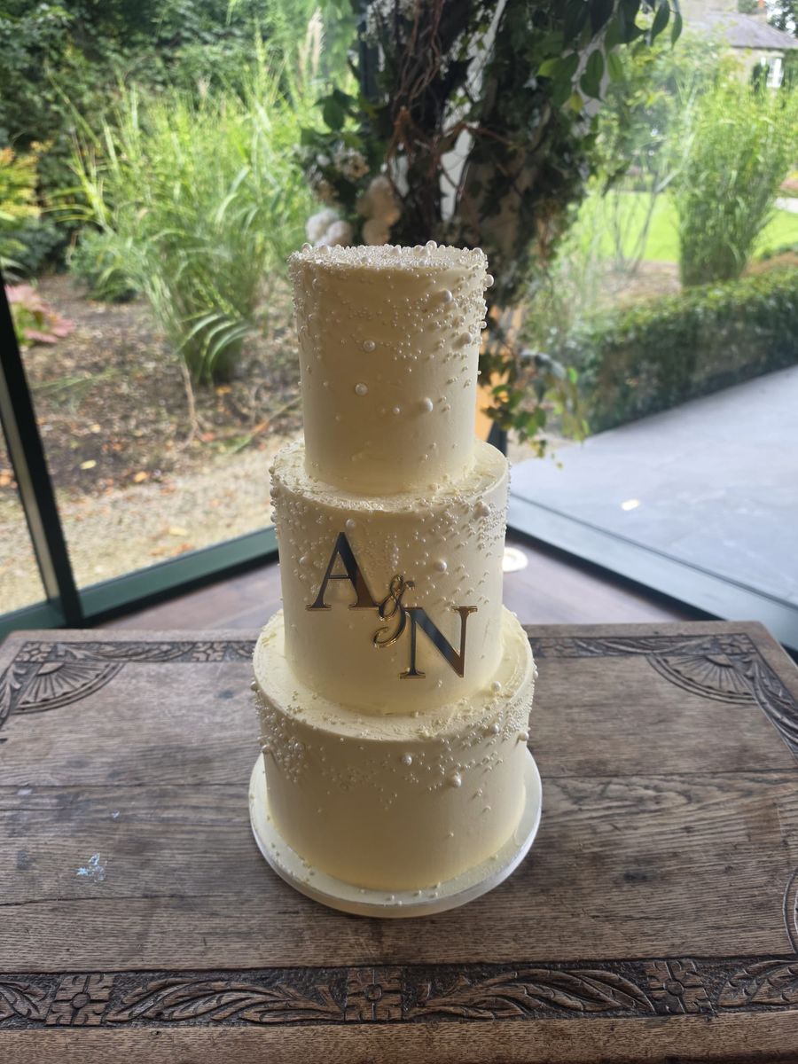 Three tier buttercream cake scattered with pearls and a gold monogram