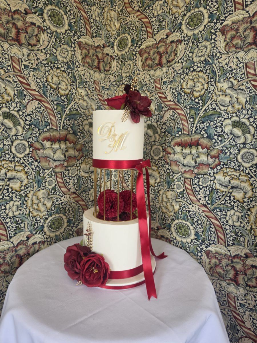 Two tier ivory wedding cake with burgundy roses, satin ribbon and a gold cage separator