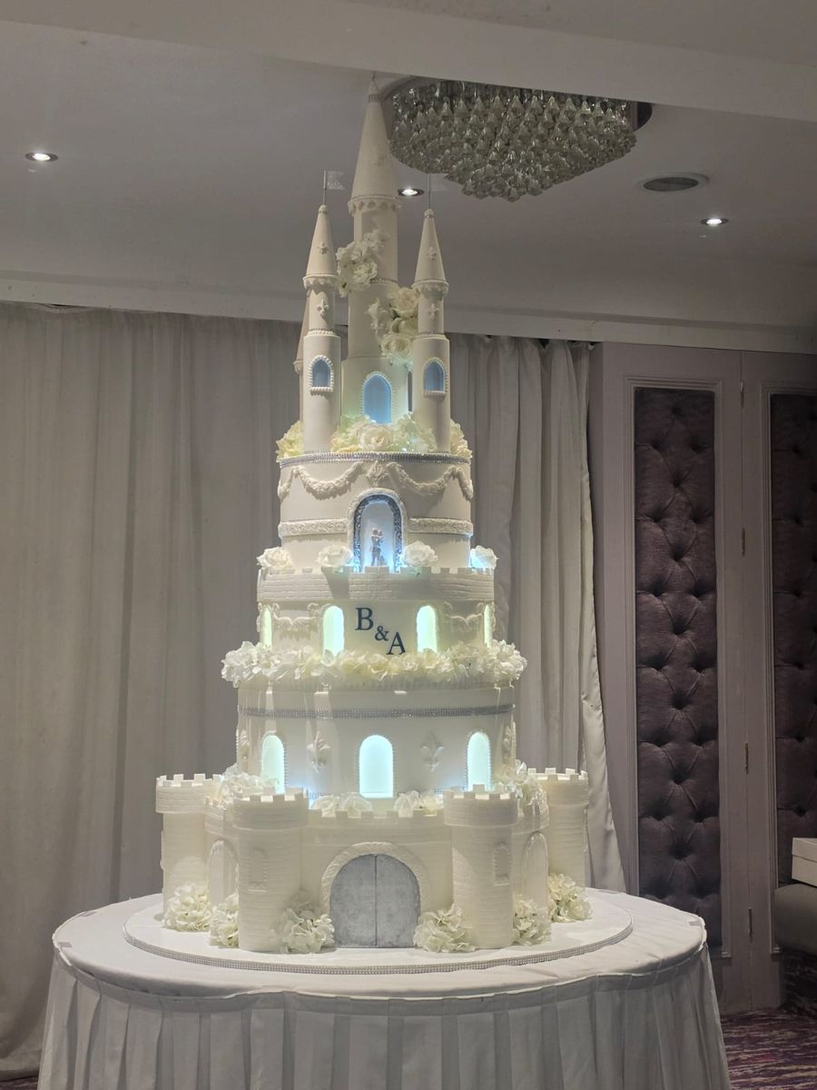 White fairytale castle wedding cake with turrets, battlements and softly lit windows