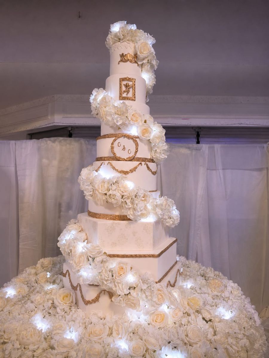 Tall white and gold wedding cake with a spiral of lit white roses and hexagonal tiers