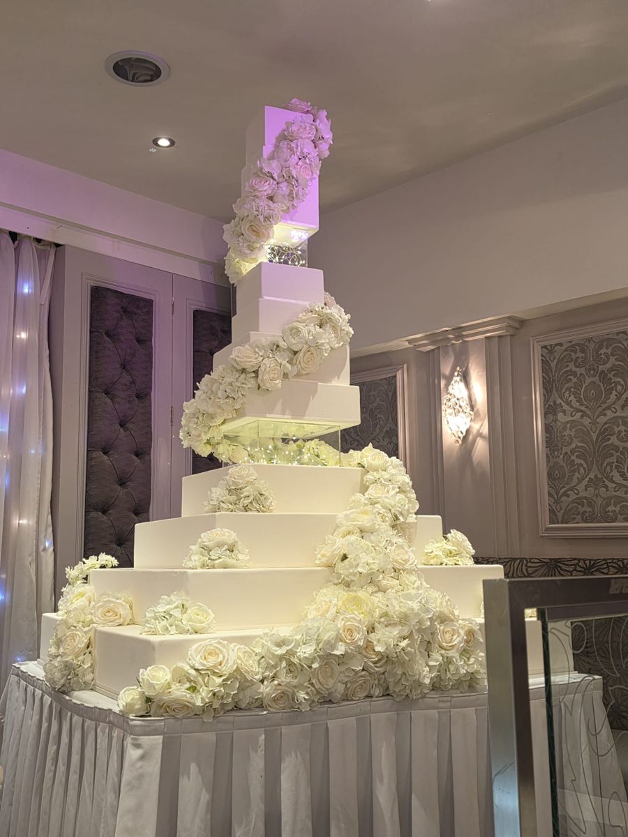 Giant square tiered wedding cake with illuminated separators and a cascade of white roses