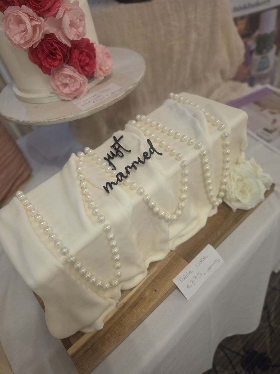 Draped white table cake with strings of pearls and a black Just Married topper